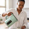Woman pouring water from 1.8L Stainless Steel Hot Water Kettle into a cup in a bright kitchen.