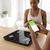 User checking health data on smartphone while using Smart Body Scale in a bright, modern setting.
