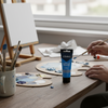 Acrylic Paint 75ml Cerulean Blue tube on a wooden table with palettes and brushes for painting.