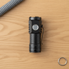 Mini Rechargeable LED Torch on a wooden surface next to a keyring and rope, showcasing its compact design.