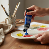 Acrylic Paint 75ml - Ultramarine being squeezed onto a palette with other colors, surrounded by painting tools.