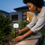 A woman installing a Multifunctional Solar Wall Lamp in her garden for enhanced outdoor lighting.
