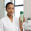 Aloe Light Brightening and Moisturising Lotion held by a woman in a bathroom setting to improve skin clarity.