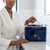 Woman in a robe holding a Patent Leather Hand-Held Toiletry Bag with a sleek design and glossy finish.