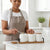 Woman in apron using Ceramic Seasoning Jar Set with Wooden Tray to measure spices in a modern kitchen.