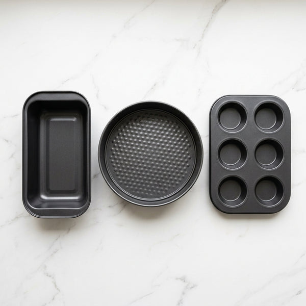 3 Piece Non Stick Bakeware Set featuring a loaf pan, round cake pan, and muffin tray on a marble surface.