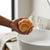 Soft Slow Rising PU Butter Stick Squishy Toy: Person holding a mesh bag of sponge balls near a wash basin in a bright kitchen.
