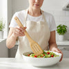 Woman using Natural House Premium Olive Wood Kitchen Utensil to serve salad in a bowl.