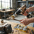Person using a drill with a wire brush attachment on a wrench in a workshop, depicting the 5 PCS Wire Brush Kit - Essential Cleaning Tool Set.
