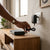 5V 2A DC Power Supply Adapter plugged into a wall outlet with a device on a wooden table.