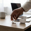 Pro6 True Wireless Waterproof Earbuds being placed on a wooden desk next to a phone and coffee cup.