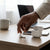 Pro6 True Wireless Waterproof Earbuds being placed on a wooden desk next to a phone and coffee cup.