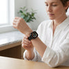 Woman checking her Waterproof Bluetooth Fitness Smartwatch while sitting at a table.