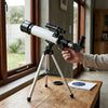 Children's High Definition Astronomical Telescope on a table with a person adjusting its settings near a window.