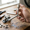 Professional Y-Type Socket Wrench held above a workbench covered with tools and hardware.
