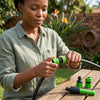 Person using the Quick Connector Garden Water Spray Gun to attach it to a garden hose in a lush outdoor setting.
