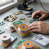 Tin Lead Rosin Core Solder Wire 100g Reel on a workstation with circuit boards and tools in use.