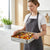 Woman holding a Non-Stick Square Carbon Steel Baking Pan filled with roasted vegetables in a modern kitchen.