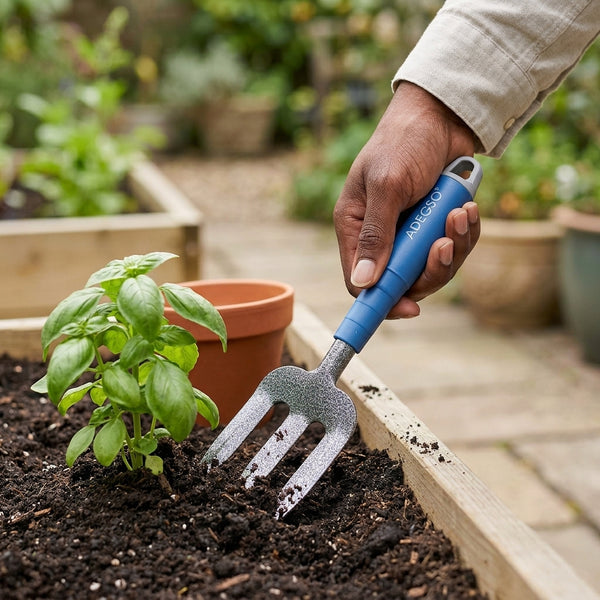 Person using an Ergonomic Heavy Duty Garden Hand Fork to tend to a basil plant in a garden bed.