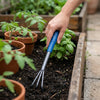 Heavy Duty 3-Prong Hand Rake being used to cultivate soil in a garden with potted plants.