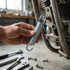 A hand holding a Blister Card Pack Extension Spring Furniture Hook near a motorcycle engine.