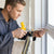 A person using a Heavy Duty Aluminous PU Foam Gun to seal a window for insulation.