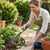 Woman using Metal Garden Lawn Rake with Telescopic Handle to tidy flower beds in a garden.