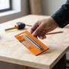 Close-up of a hand holding a High-Quality Planer Blade Set package on a wood surface, with tools in the background.