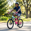 A young boy riding a Multi-Color Hardtail Mountain Bike on a sunny trail, wearing a helmet and enjoying his ride.