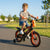 A happy child riding the Carbon Steel Kids Training Bike in a park, showcasing its vibrant design and stability.