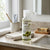 Natural Extract Moisturizing Olive Oil bottle on a bathroom countertop with towels and soap.