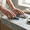 Person using Ear Wax Removal Camera Kit with LED Light next to a smartphone on a marble countertop.