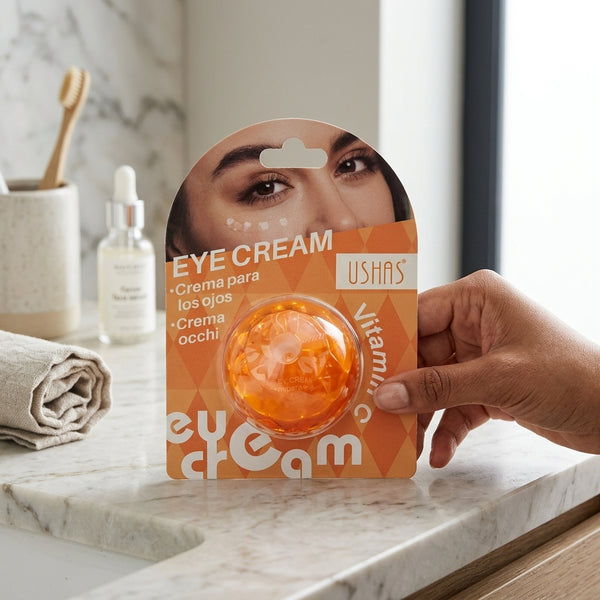 Vitamin C Brightening Under Eye Patches in an eye cream package held by a hand on a marble countertop.
