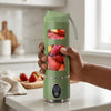 Person holding a Mini USB Rechargeable Portable Blender filled with fresh fruits on a kitchen counter.
