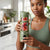 Woman holding a Mini USB Rechargeable Portable Blender filled with fresh fruits in a modern kitchen.