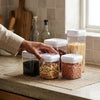 Easy Button Round Kitchen Storage Jar with dry ingredients like nuts and pasta, organized on a kitchen countertop.