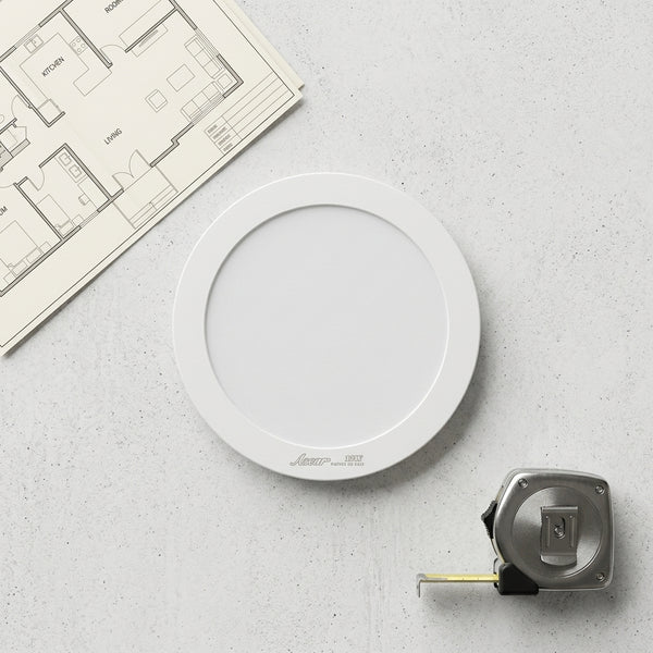12W Round LED Surface Panel Light on a countertop next to a floor plan and a tape measure.