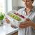Woman holding a 2 Section Plastic Snack Storage Container with Lid filled with grapes and cherries.