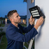 A person installing a 150W Outdoor Solar LED Floodlight on a wall, showcasing its outdoor use.