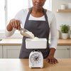 Woman measuring flour with Mechanical Kitchen Scale 1kg in modern kitchen.