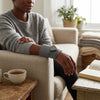 Person relaxing on a couch using the Joint Heating Vibration Massage Wrap on their arm while enjoying a cup of tea.