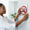 Person installing a No Smoking Sign on a wall to promote a smoke-free environment.