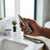Rechargeable Mini Nose and Ear Hair Trimmer held in hand near a bathroom sink with grooming accessories.