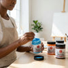 Artist using Professional Vivid Acrylic Paint 250ml jars on a wooden table with paintbrushes.