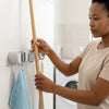Woman organizing cleaning tools with Wall Mounted 3 Hook Mop and Broom Hanging Rack in the laundry room.