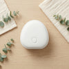 Portable White Noise Sound Machine on a wooden surface, surrounded by eucalyptus leaves and soft fabric.