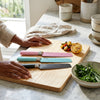 Velvet-Touch Pastel Precision Knife set displayed on a wooden cutting board with fresh ingredients.