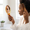 Woman using the Classic Mirror and Comb Grooming Set in a bright bathroom, styling her hair with a tortoiseshell comb.