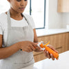 A person using a Cute Cartoon Carrot Vegetable Y-Peeler to peel a carrot in a modern kitchen.