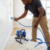 Man using an Airless Paint Sprayer for smooth wall painting in a well-lit room.